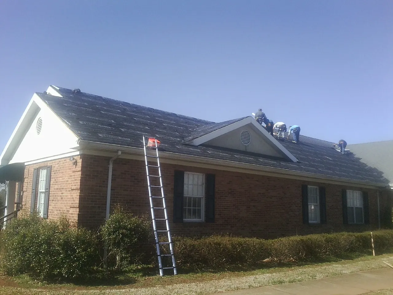 Crew tearing shingles off a brick ranch roof with a ladder set — Emergency Roof Repair work by our crew in Vandalia
