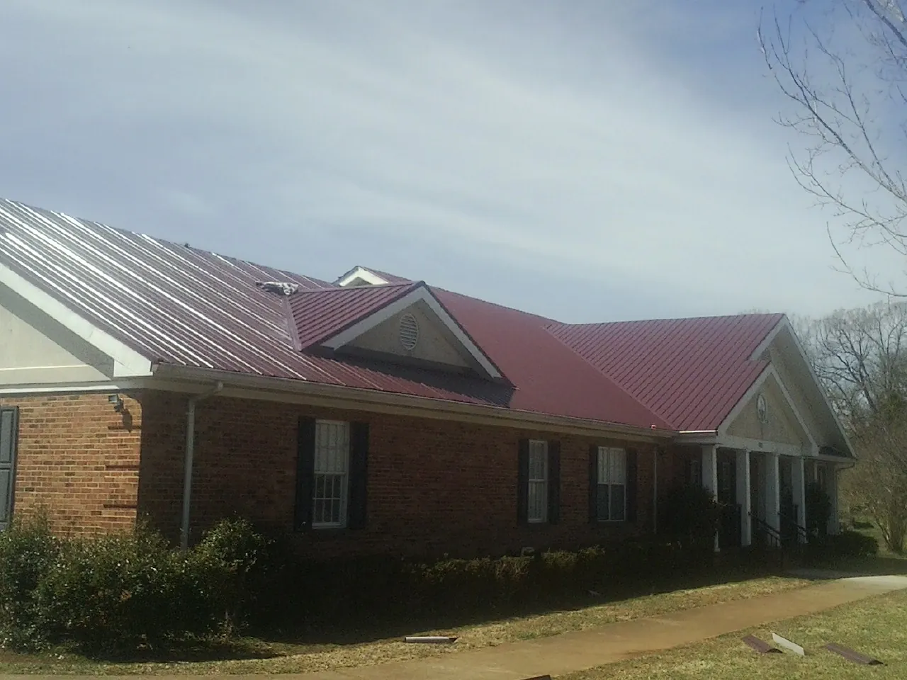 Red metal roof with gabled entries on a long brick building, from a Hail Damage Roof Repair job in Vandalia