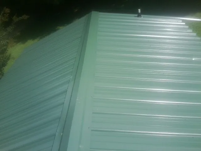 New green metal panels meeting at the ridge of a roof — Flat Roof Repair work by our crew in Vandalia