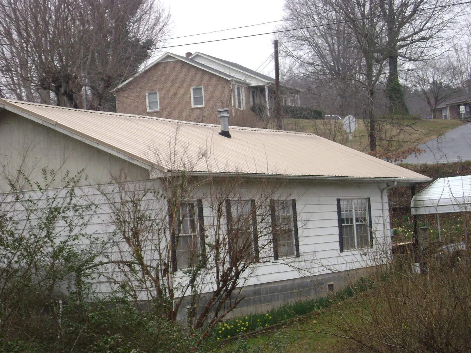 Tan metal roof on a white sided house set into a hillside — Commercial Roofing by Roofing Brothers in Vandalia